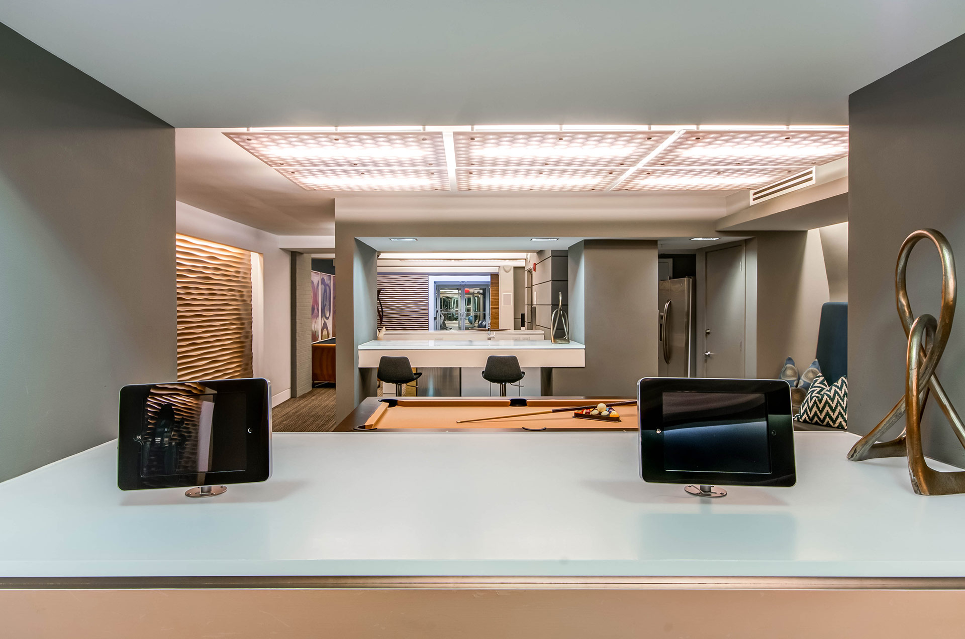 Computer bar closeup of community smart tablets with view to pool table and seating down the hall