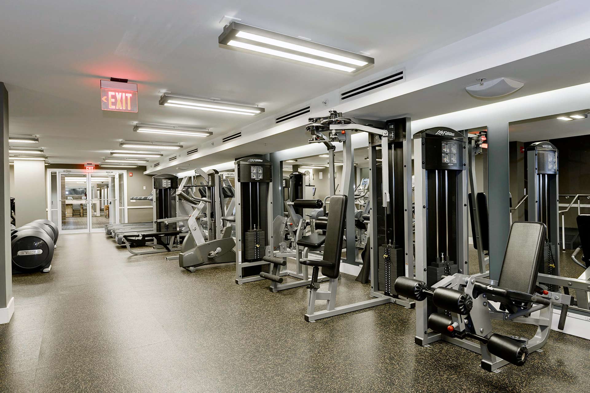 Large fitness room with impact absorbent flooring and strength training equipment along the right, mirrored wall