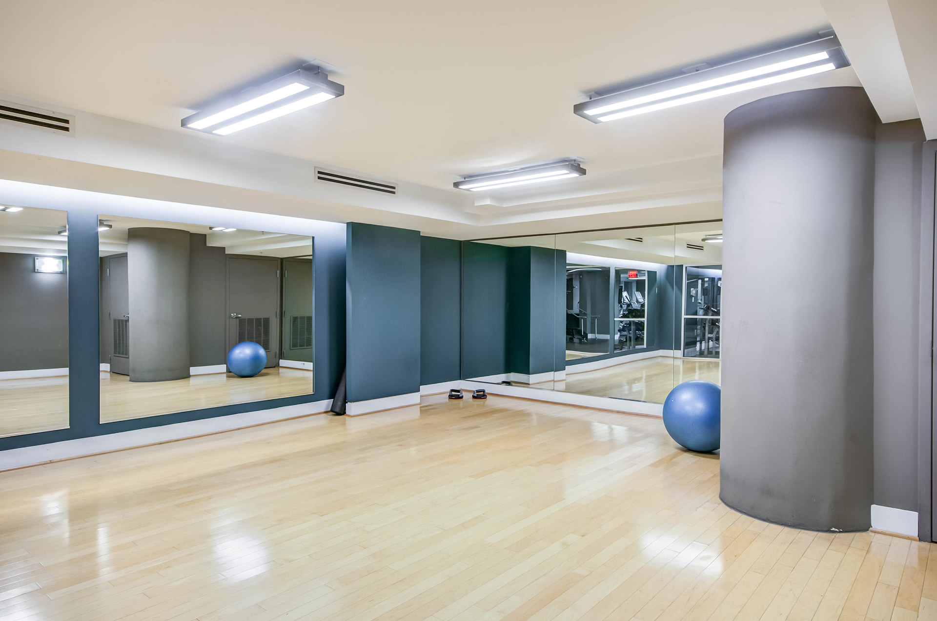 Clean and bright yoga and stretch studio with light wood flooring, mirrored walls and basic equipment stored to the right
