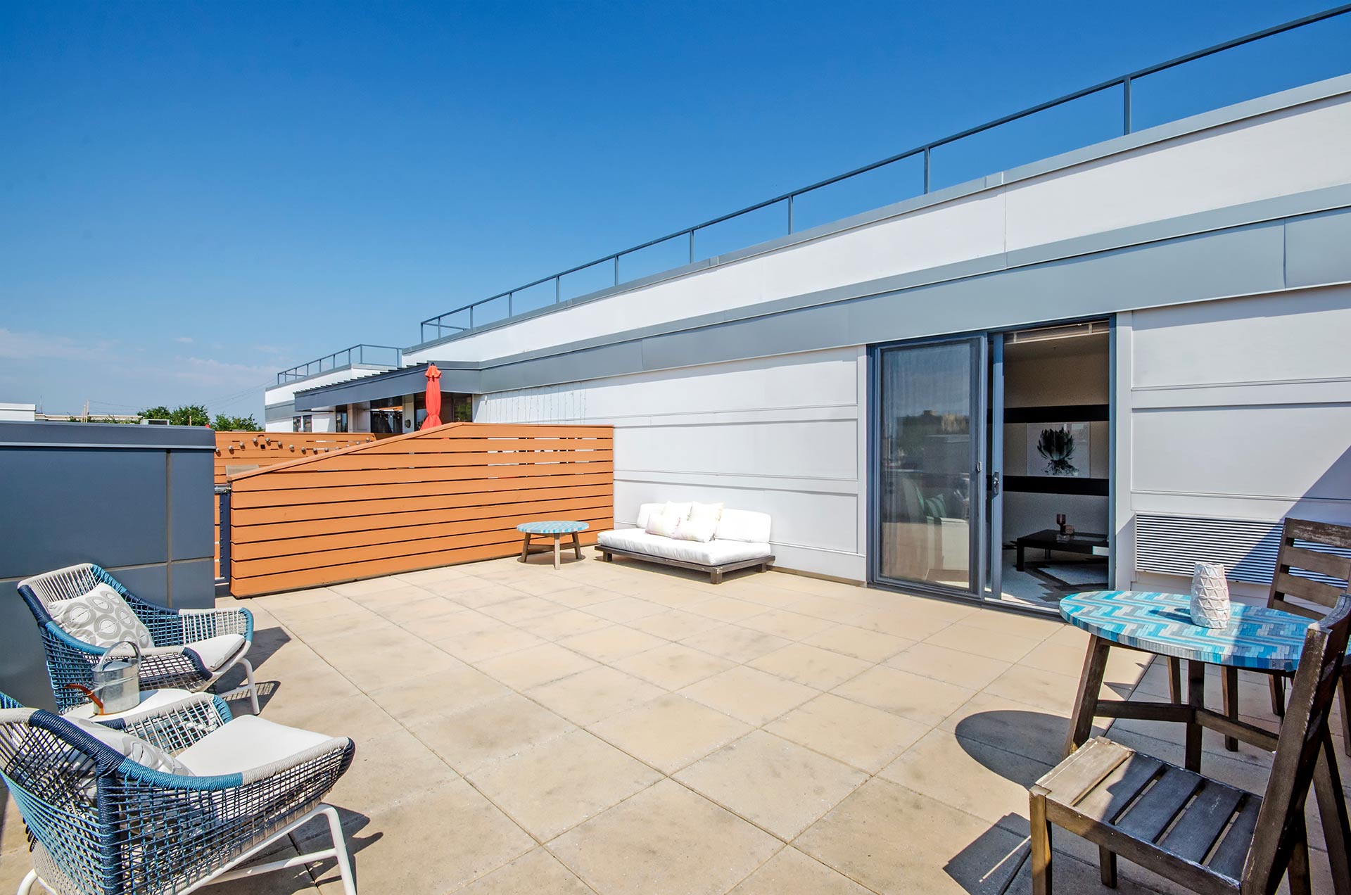 Expansive shot of outdoor furniture on private roof terrace with sliding doors open to apartment loft space inside